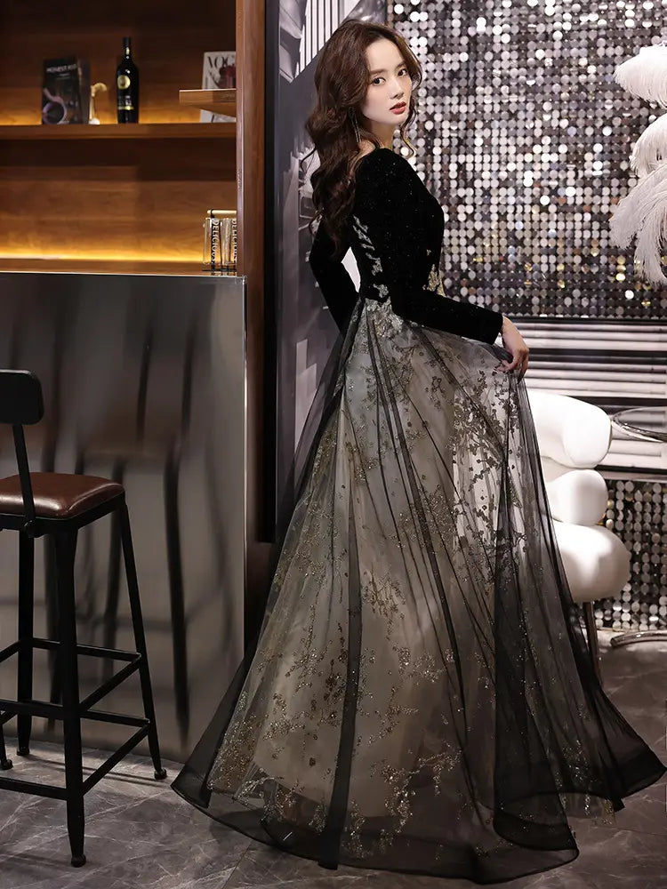 Black moderator long velvet gown featuring sheer gold-embroidered skirt and long sleeve design for annual party events.