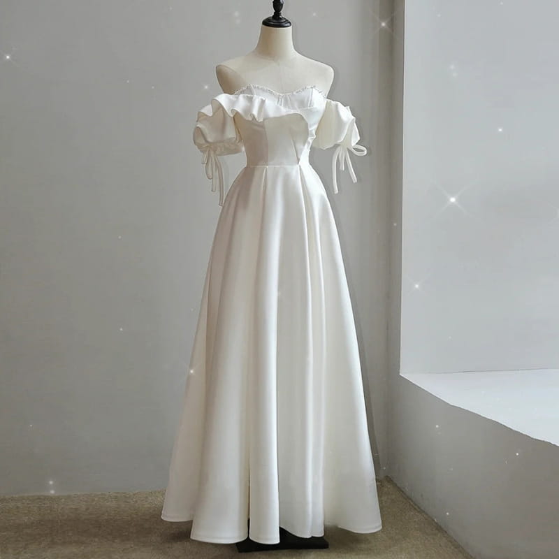 A flowing white satin light wedding dress with off the shoulder neckline, puffed sleeves, and delicate tie details for the wedding dress bride.