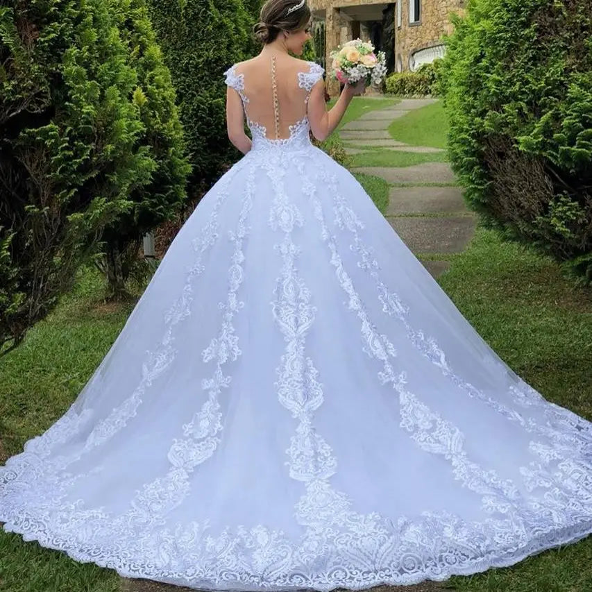 A flowing white lace wedding dress white featuring an intricate back design and a voluminous floral train made from vintage lace main fabric.