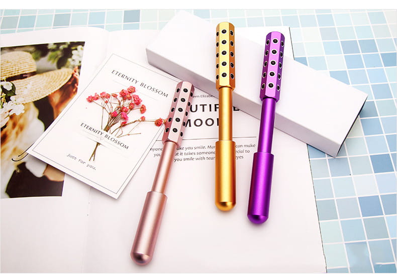 Three metallic germanium beauty roller massage sticks in rose gold gold and purple with black dot patterns for facial massage and skincare.