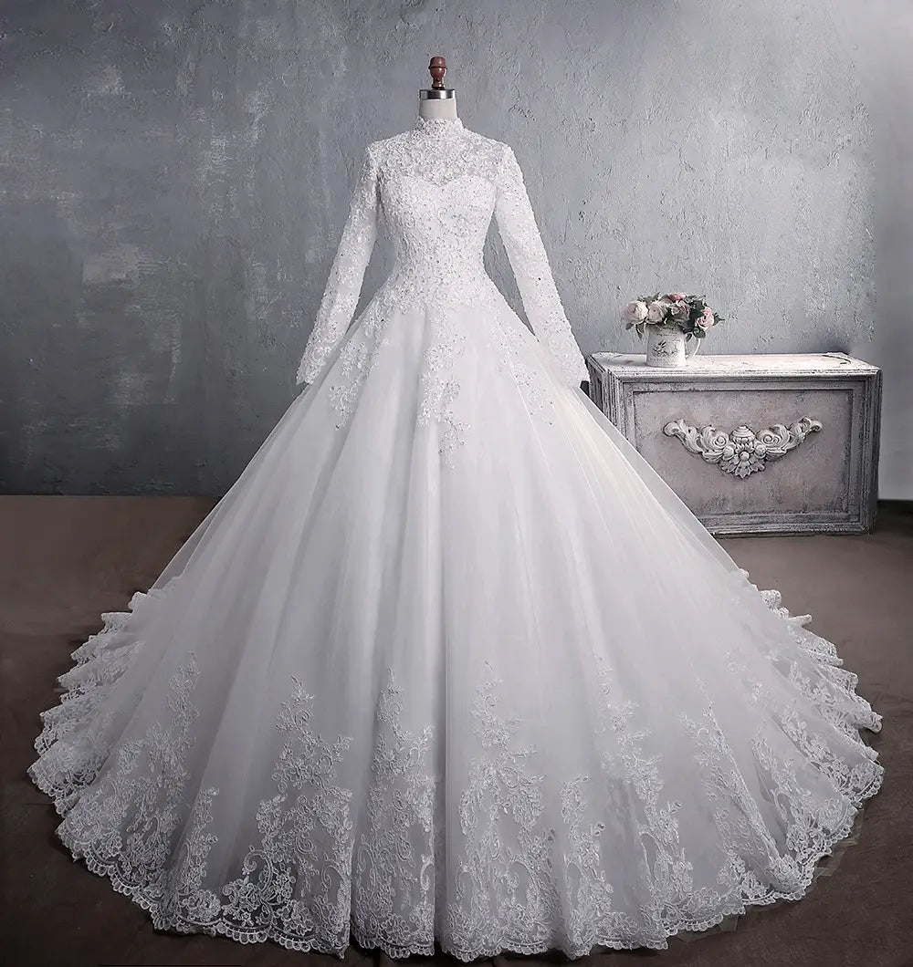 Long sleeve lace wedding dress bridal gown in white featuring a high neckline, intricate floral embroidery on the bodice and skirt hem, and a large tail.