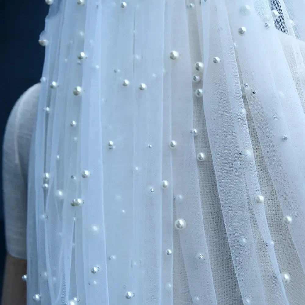 A delicate white tulle luxury heavy industry bridal veil adorned with scattered pearl-like beads and tiny silver accents paired with a tiara.