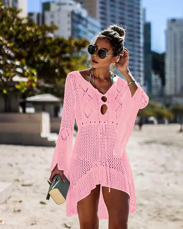 Pink knitted beach cover-up with a v-neck, eyelet details, and asymmetrical hem designed as a women swimsuit cover-up dress for bikini women.