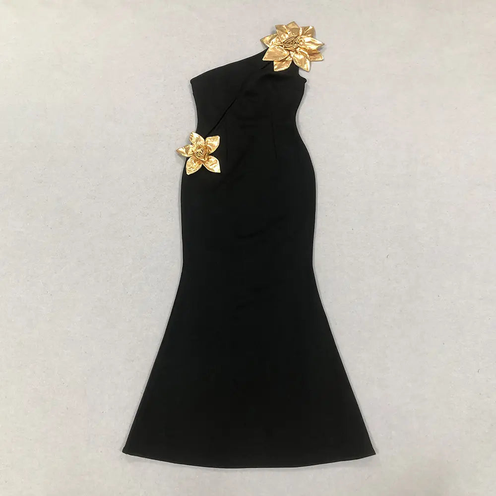 Black satin bandage golden flower maxi dress featuring a black one-shoulder mermaid silhouette adorned with two golden floral embellishments.