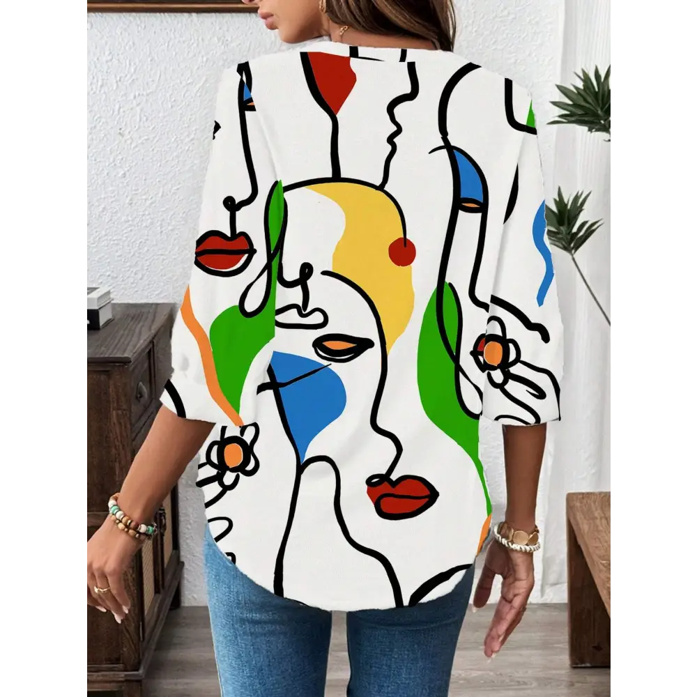White casual office blouse with abstract face pattern in black outlines and bold red yellow green blue accents and long sleeves