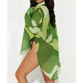 A sheer green camouflage beach cover-up with side tie paired with an abstract pink and orange printed bikini blouse