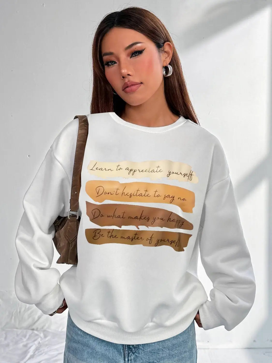 White oversized long sleeve sweatshirt in solid colour with motivational quotes printed in brown and beige on horizontal stripes, ideal for daily wear.