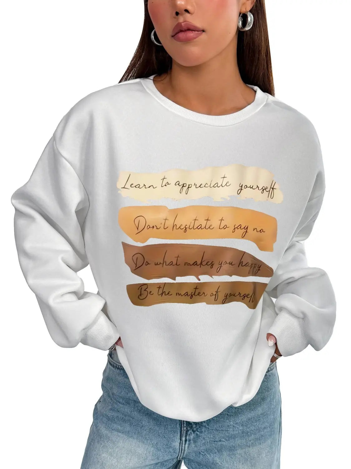 White oversized long sleeve sweatshirt in solid colour with motivational quotes printed in brown cursive on layered textured beige and tan horizontal strips suitable for daily wear.