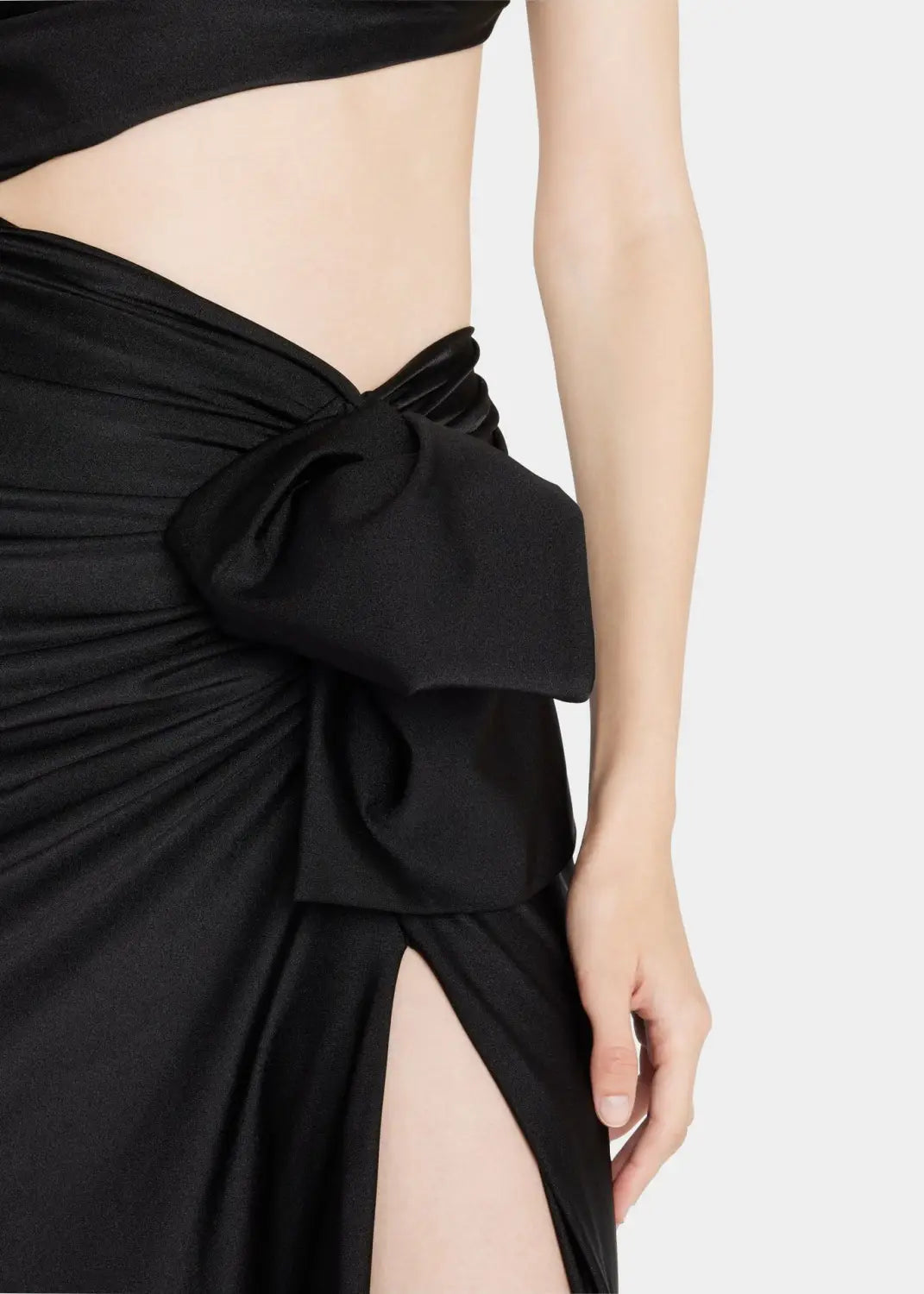 black satin skirt with a prominent twisted bow at the waist featured in a long sleeved hollow slit elastic shoulder dress showcasing the sleeved hollow slit design and elegant material.