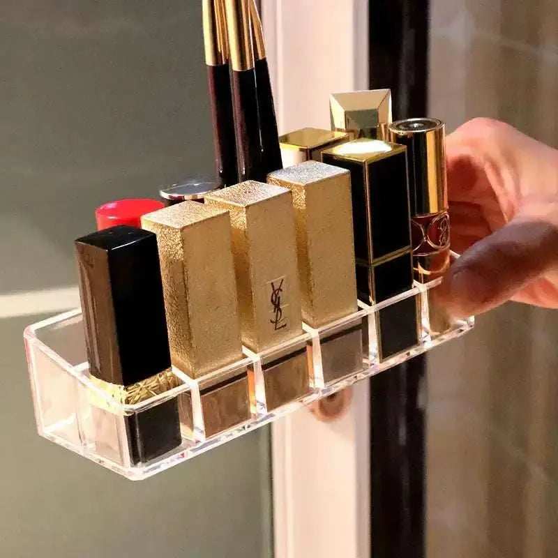 Clear acrylic makeup organizer with compartments holding multiple luxury lipsticks in gold and black cases