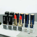 Clear acrylic makeup organizer with compartments holding multiple black and navy blue biaqua and novo silk ture lipsticks with gold caps