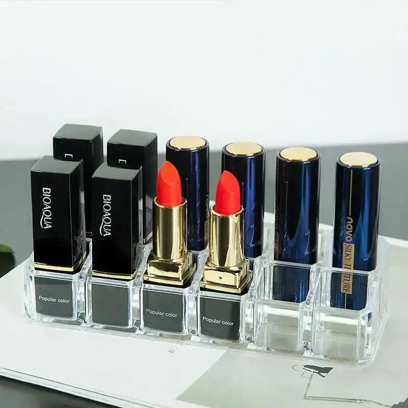Clear acrylic makeup organizer with compartments holding multiple black and navy blue biaqua and novo silk ture lipsticks with gold caps