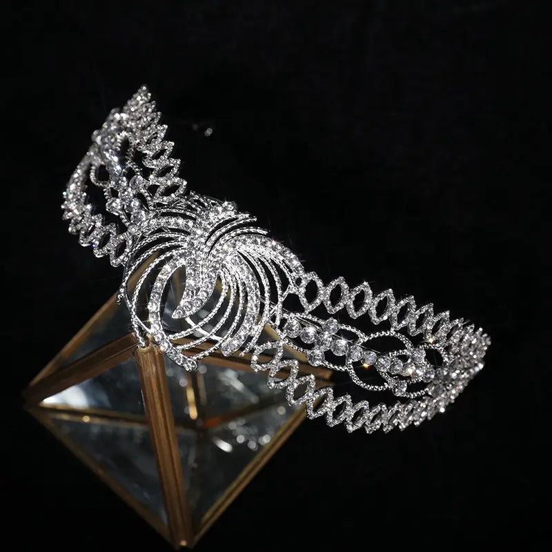 A sparkling silver rhinestone crown luxury with intricate crystal embellishments and a swirling phoenix motif design for luxury clothing bridal use.
