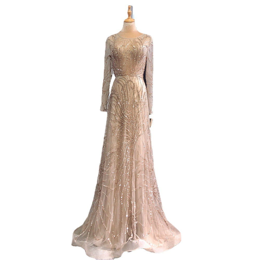 A shimmering champagne-colored light luxury minority evening gown with long sleeves and intricate beaded detailing flowing gracefully from the bodice to the floor.