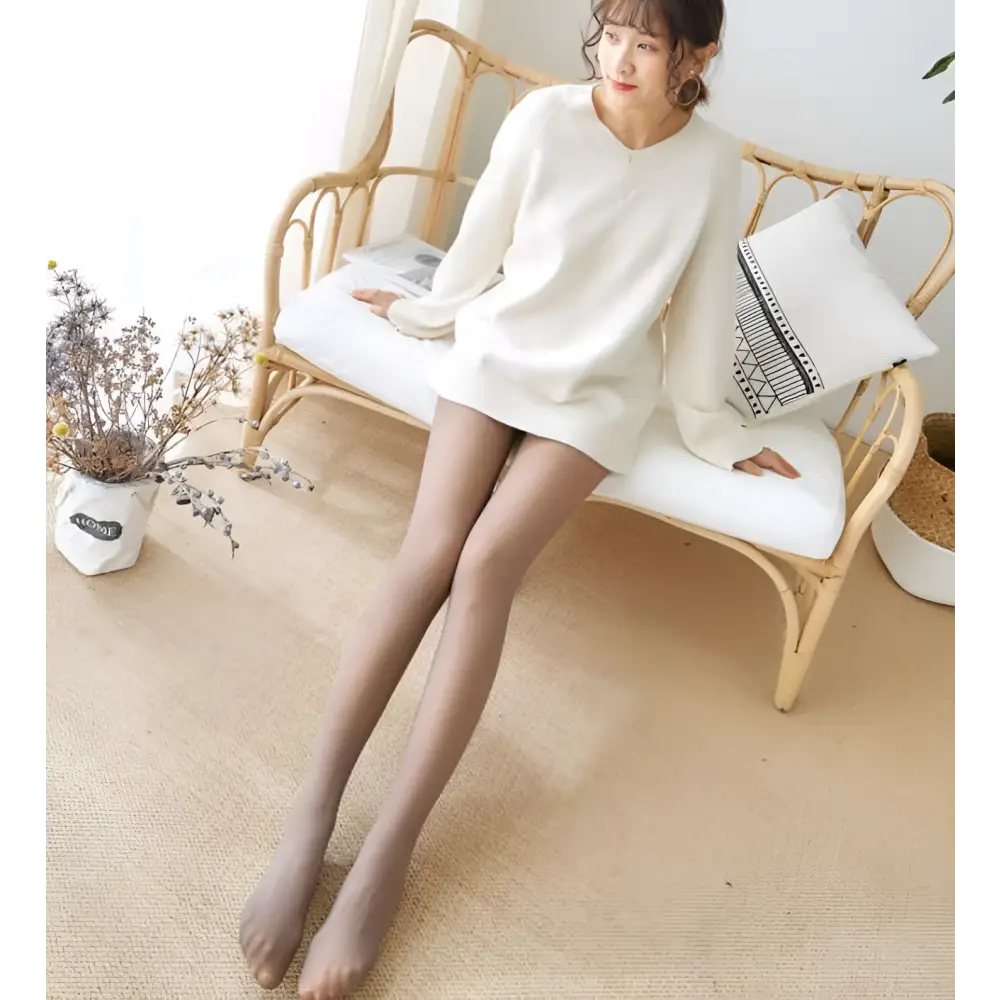 A woman seated on a rattan bench wearing sheer skin-toned adjustable maternity pantyhose tights for comfort