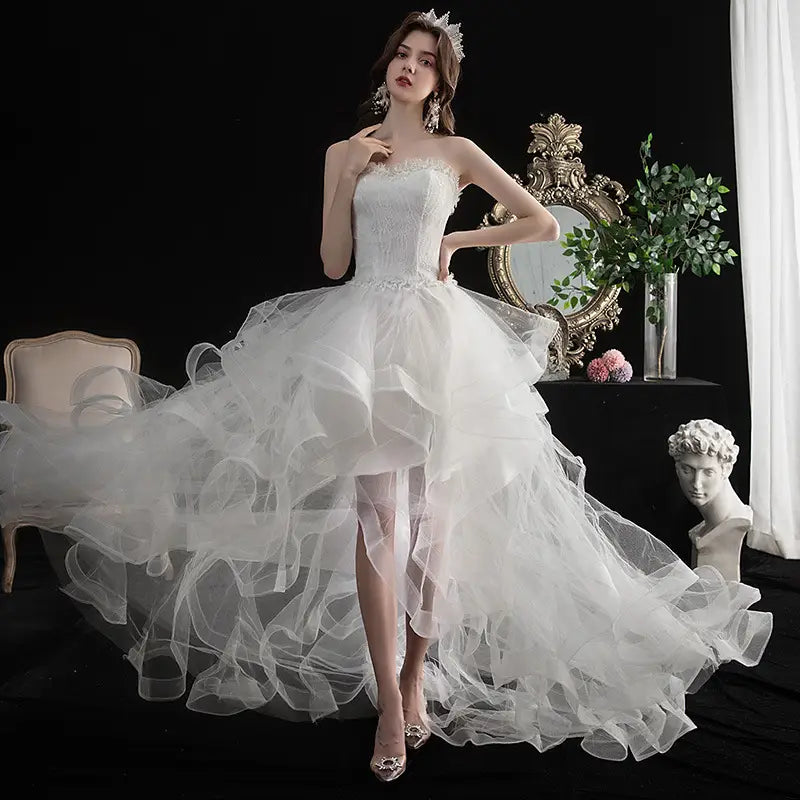A flowing white small trailing wedding dress with intricate lace detailing and a voluminous layered tulle skirt.