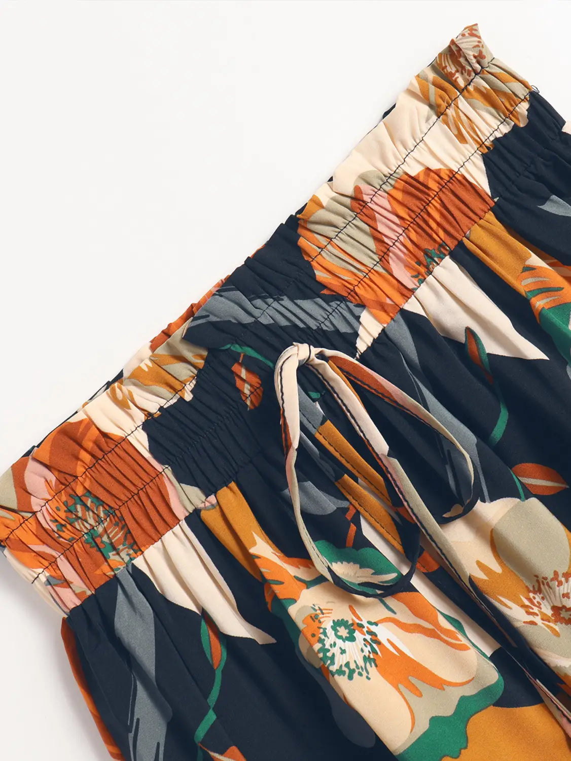 a pair of high-waisted shorts in a vibrant pleated floral print with bold orange cream and green blossoms on a dark navy floral print elastic waist.