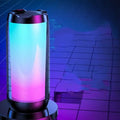 A sleek cylindrical led ambient light gaming bluetooth speaker with black frame and teal to pink gradient lighting