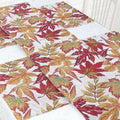 A woven decor table runner with a vibrant autumn maple leaf pattern in red orange and gold on white background
