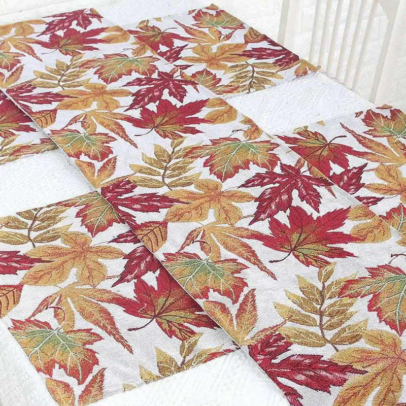 A woven decor table runner with a vibrant autumn maple leaf pattern in red orange and gold on white background