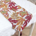 A woven autumn maple leaf decor table runner with vibrant red orange and gold leaves on a white background