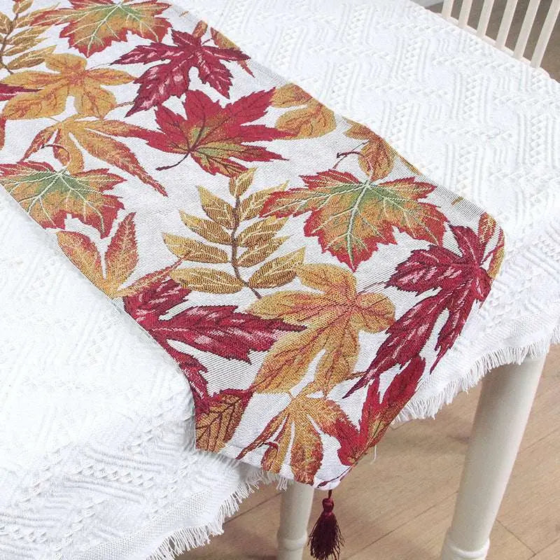 A woven autumn maple leaf decor table runner with vibrant red orange and gold leaves on a white background