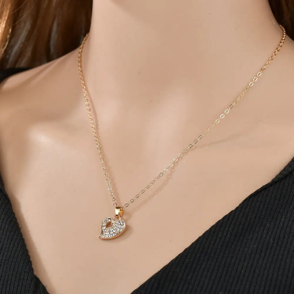 A delicate gold-toned necklace with a heart-shaped pendant adorned with sparkling clear crystals from the gold rhinestone heart love jewelry set.