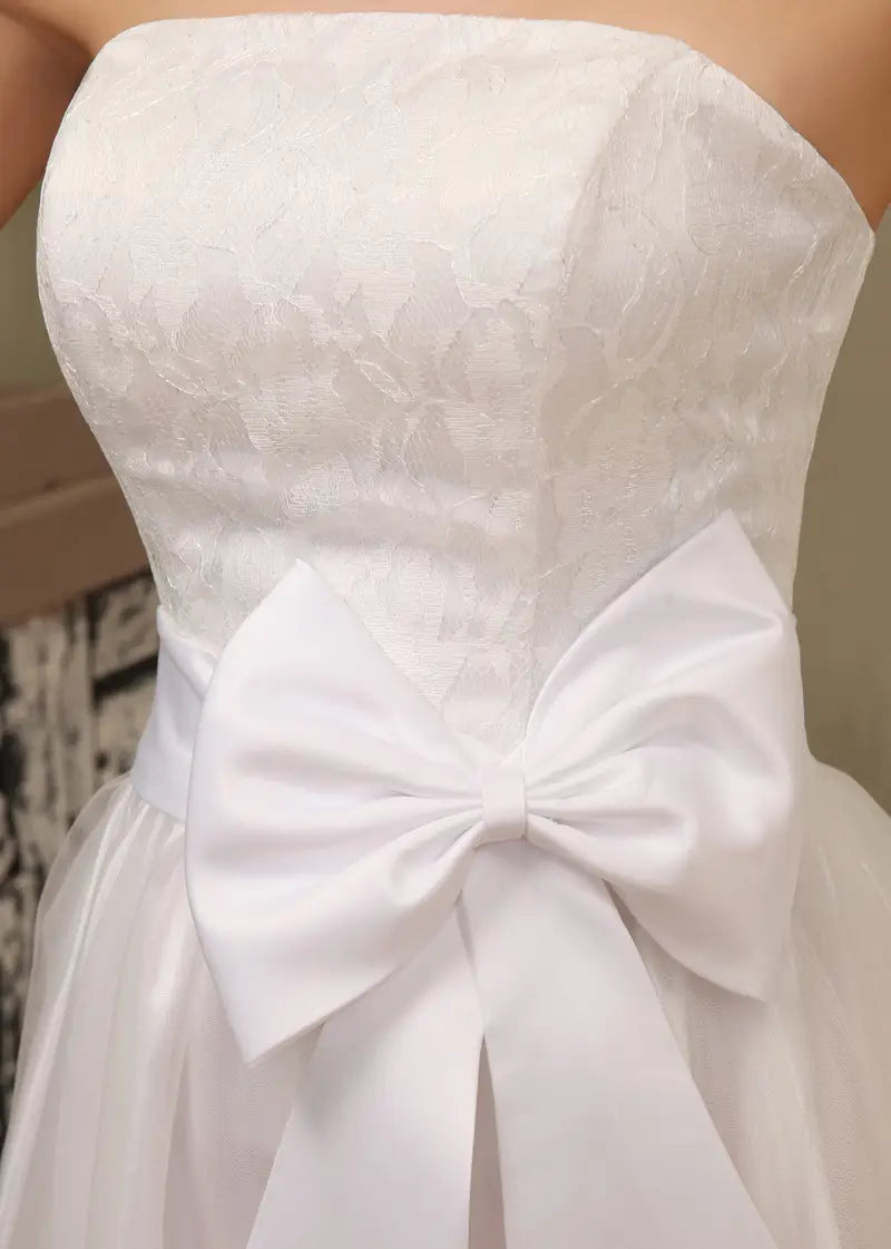 short tube bride wedding dress in white lace with a strapless design and a large satin bow at the waist