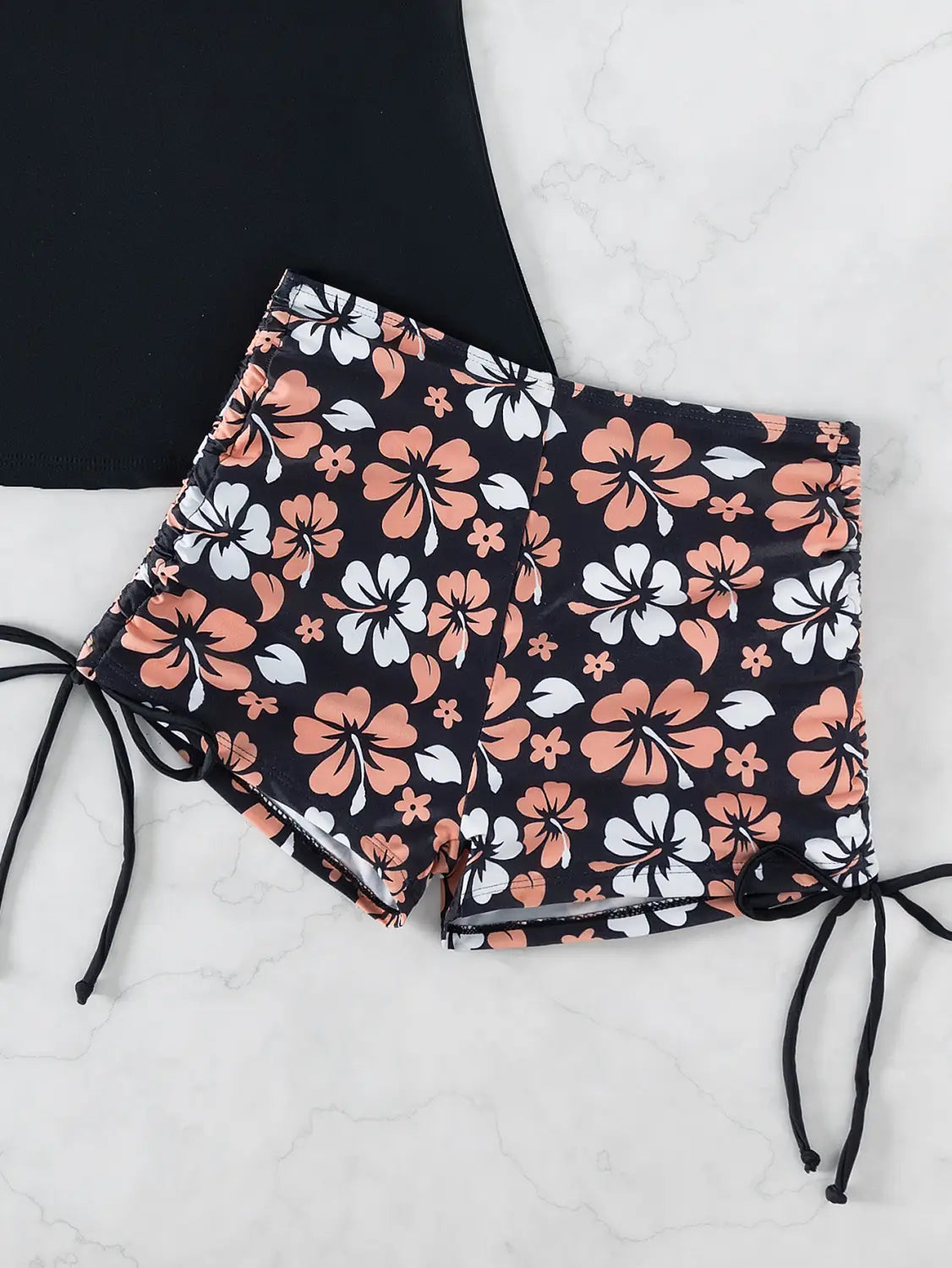 black shorts with a vibrant floral pattern featuring peach and white hibiscus flowers and black drawstrings at the sides, part of a floral halterneck printed halter bikini split swimsuit.