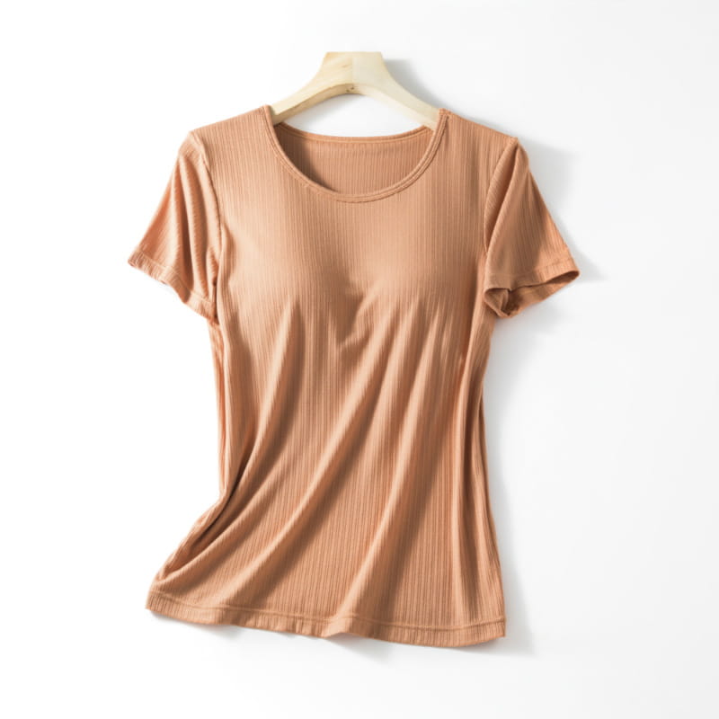A soft peach-colored ribbed cotton women’s summerdale loose-fitting padded chest t-shirt with a round neckline and short sleeves hanging neatly on a wooden hanger.