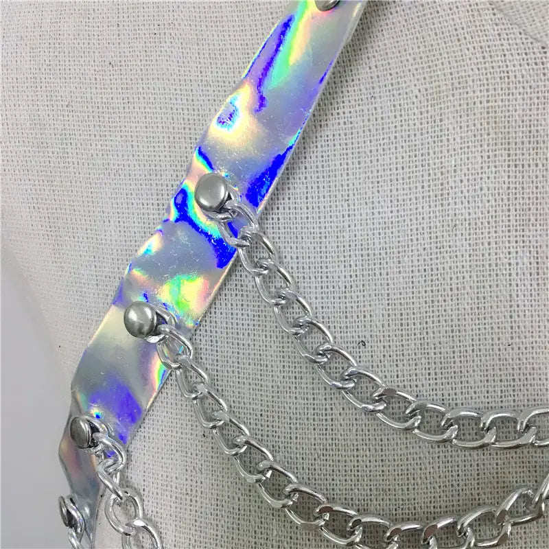 a creative versatile laser ladies belt bodysuit featuring a shimmering holographic strap with silver-toned metal hardware and chain displaying iridescent rainbow reflections across its surface