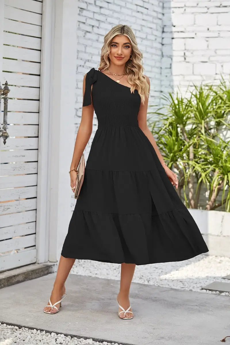 Black one-shoulder tiered midi dress with a ribbed bodice and flowing skirt featuring a pleated layered hem and hem split dress design.