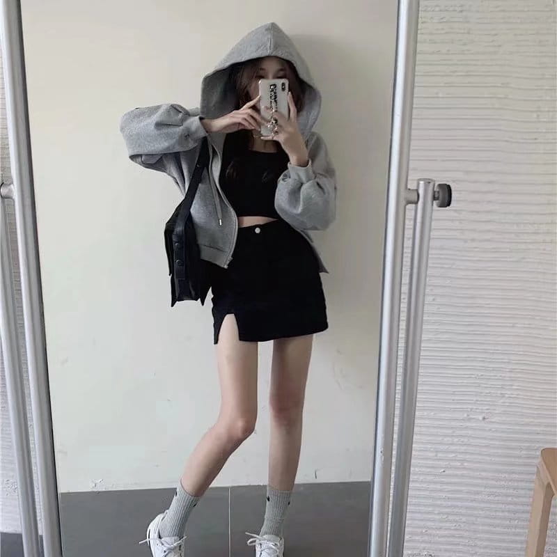 gray hooded zip-up jacket with relaxed fit and ribbed cuffs paired with distressed black denim skirt featuring a side slit