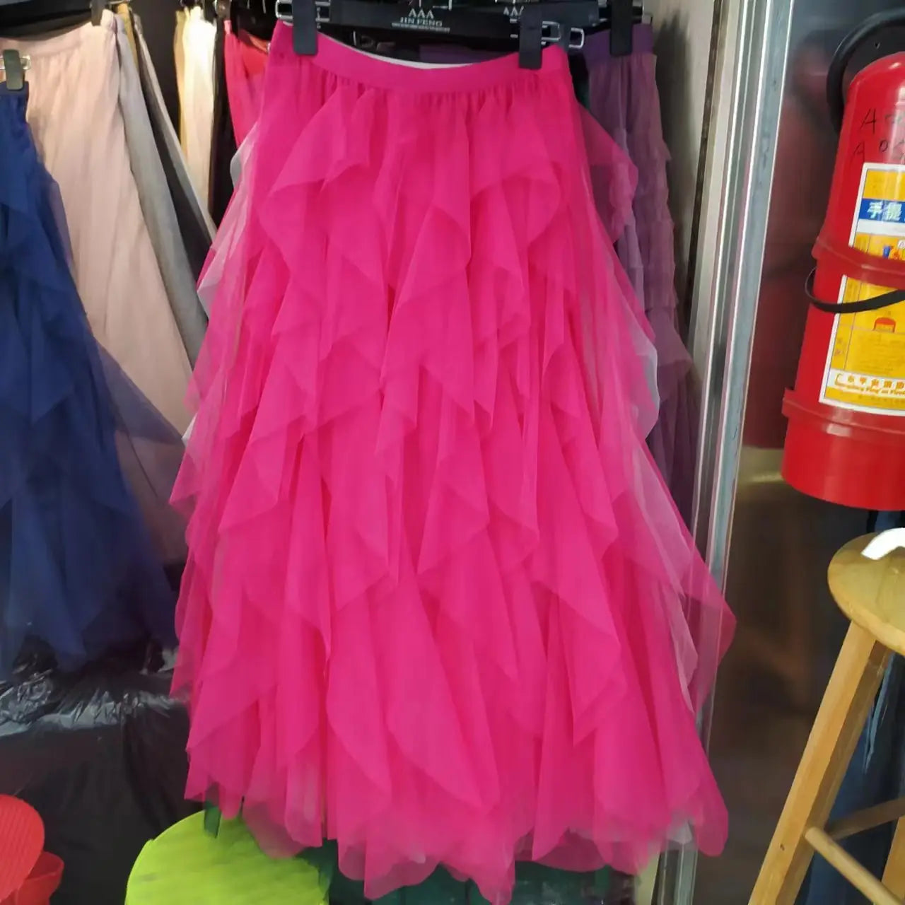 A vibrant fuchsia tiered tulle skirt with multiple ruffled layers hanging on a black hanger showcasing easy matching mesh stitching features.