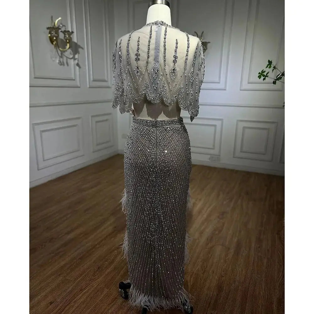 A shimmering silver nude evening dress featuring intricate beading, feather trim, and a sheer embellished capelet designed for elegant occasions.