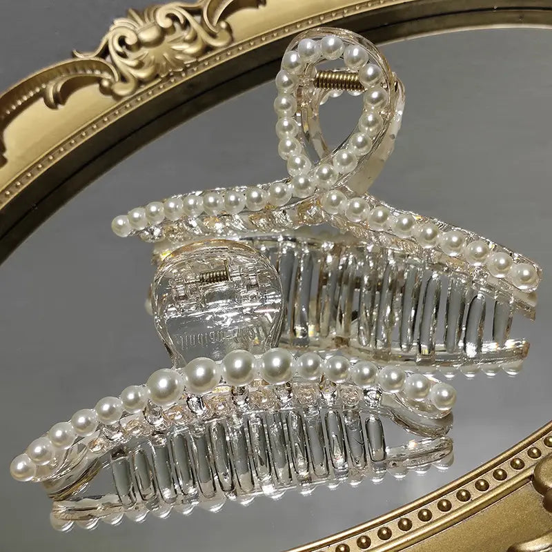 Transparent pearl grab clip made of clear acrylic adorned with a row of white pearls along its curved frame featuring a rhinestone bow for a gentle and elegant hold.