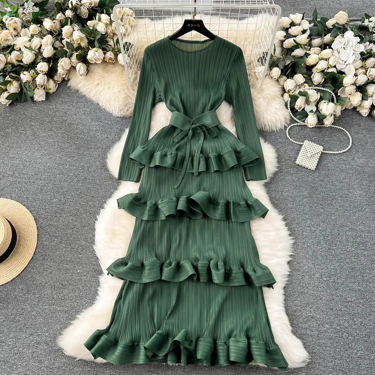 a long-sleeved emerald green heavy industry pleated long dress featuring tiered ruffles and a matching belt from the cake heavy industry collection