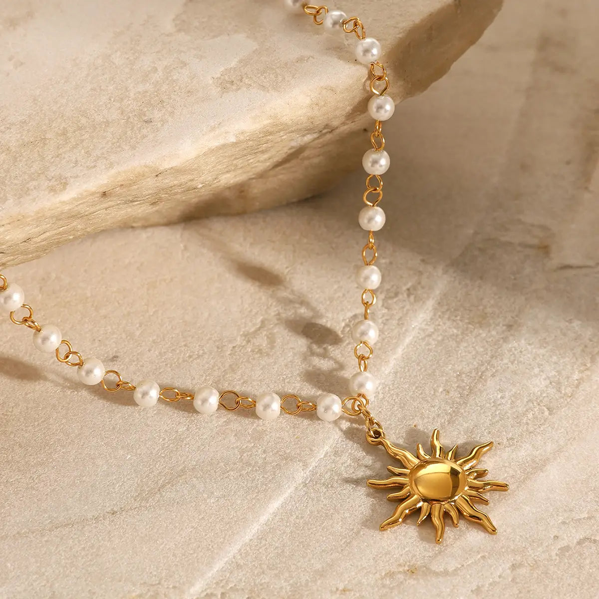 A stainless steel pearl necklace featuring a delicate gold sun pendant adorned with a string of white pearls linked by fine golden chains.