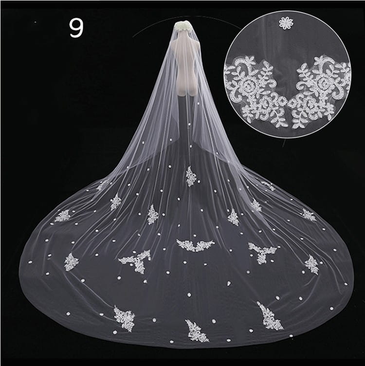 A delicate sheer white wide style bridal wedding dress veil with intricate lace floral patterns and pearl-like embellishments featuring a hair comb.