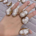 A hand wearing a gold-toned necklace ring suit with large white baroque pearls and clear crystals as bride ornament