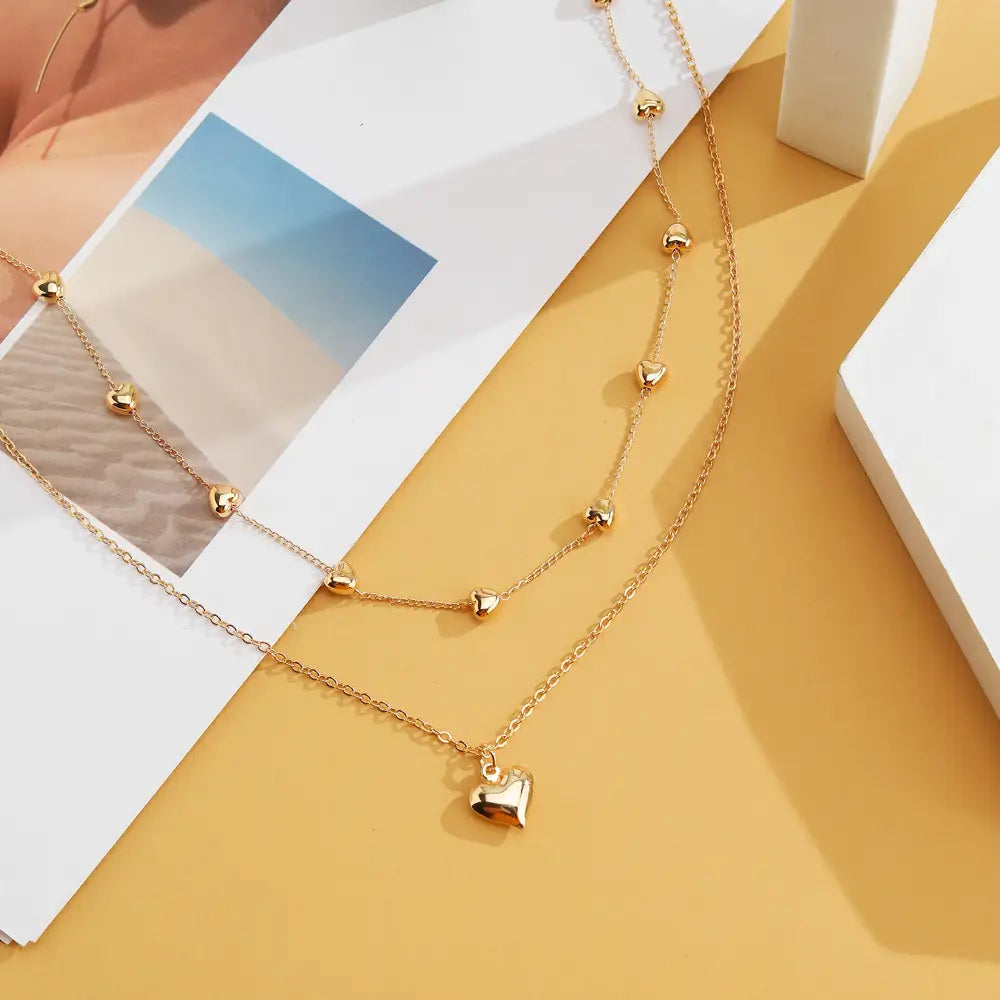 Gold-toned double layer heart pendant fine chain necklace featuring delicate chains with small heart-shaped charms and a larger dangling heart pendant.