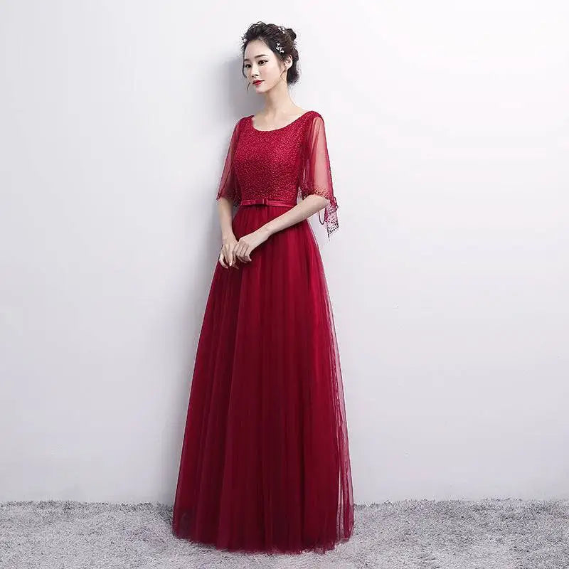 A woman wearing a deep red banquet evening dress with an embellished bodice and sheer three-quarter sleeves