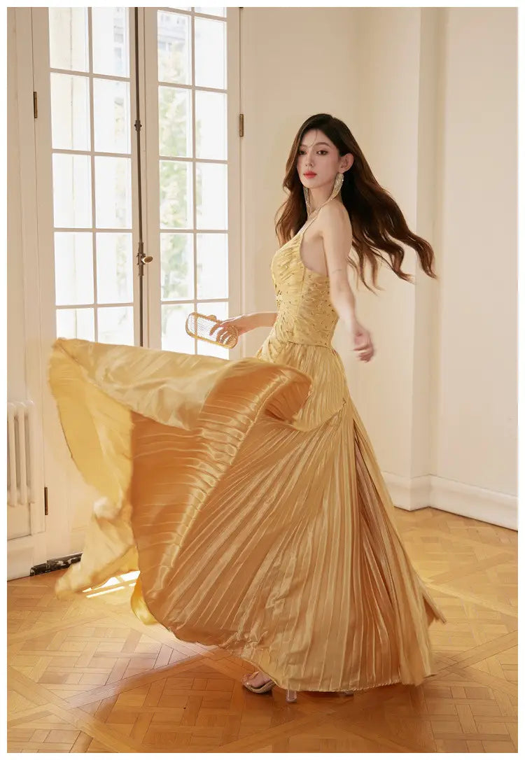 A flowing gold satin heavy industry birthday dress featuring a pleated gown design with a halter neckline and intricate beaded detailing.