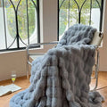A plush beige rabbit velvet blanket thickened with light gray faux fur throw and quilted texture draped on a chair