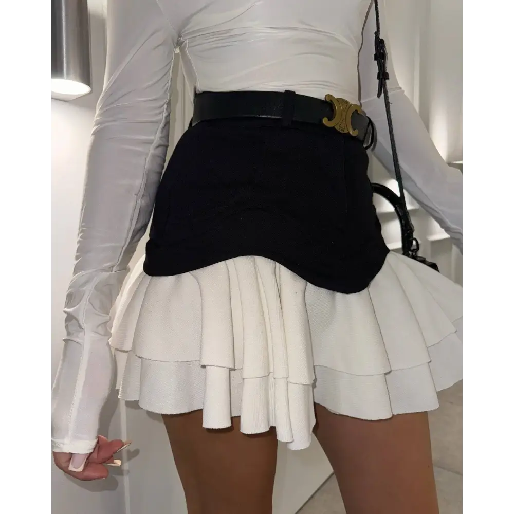 Black leather belt with gold-tone c-shaped buckle paired with beige two tone ruffled high waist tiered skirt