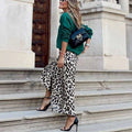 Black leather crossbody bag with gold-tone logo and chain strap paired with leopard print elastic a line skirt with flared hem