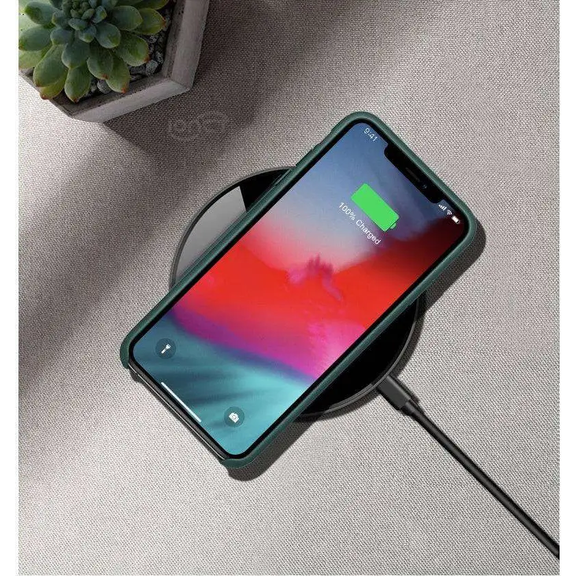 A sleek green phone case on a black glossy 15w smooth wireless charger showing 100% charged on screen