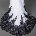 A flowing white slim mermaid tail wedding dress with intricate black lace detailing along the hemline
