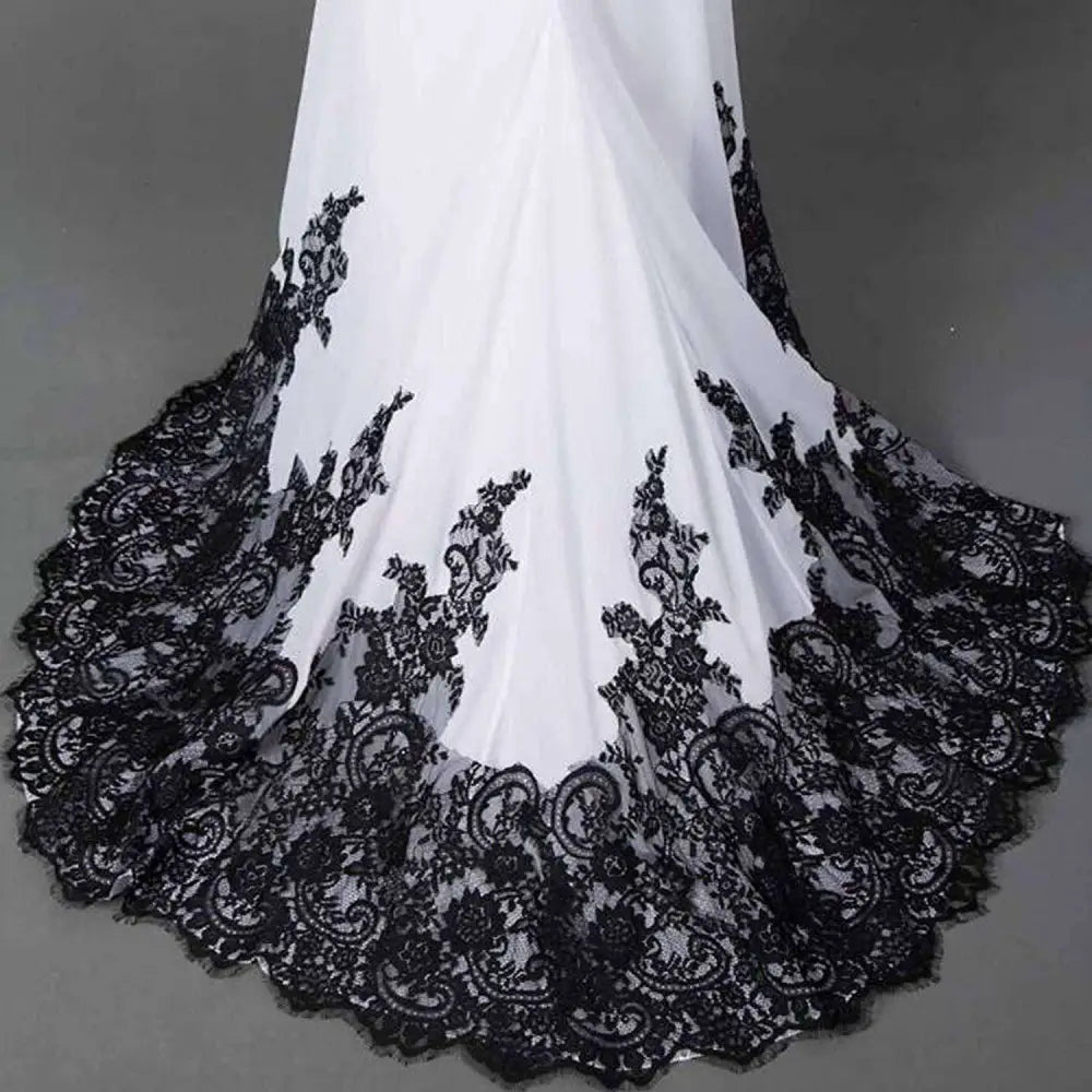 A flowing white slim mermaid tail wedding dress with intricate black lace detailing along the hemline