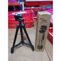 Black portable tripod universal digital camera bracket with adjustable legs standing next to cardboard box labeled tripod 3120 made in china